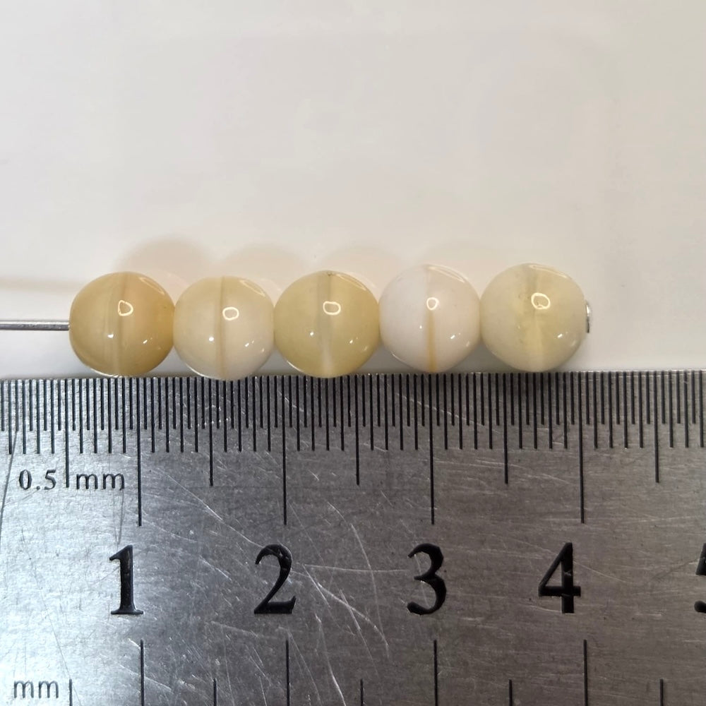 five cream beige round glass beads with a ruler to show scale