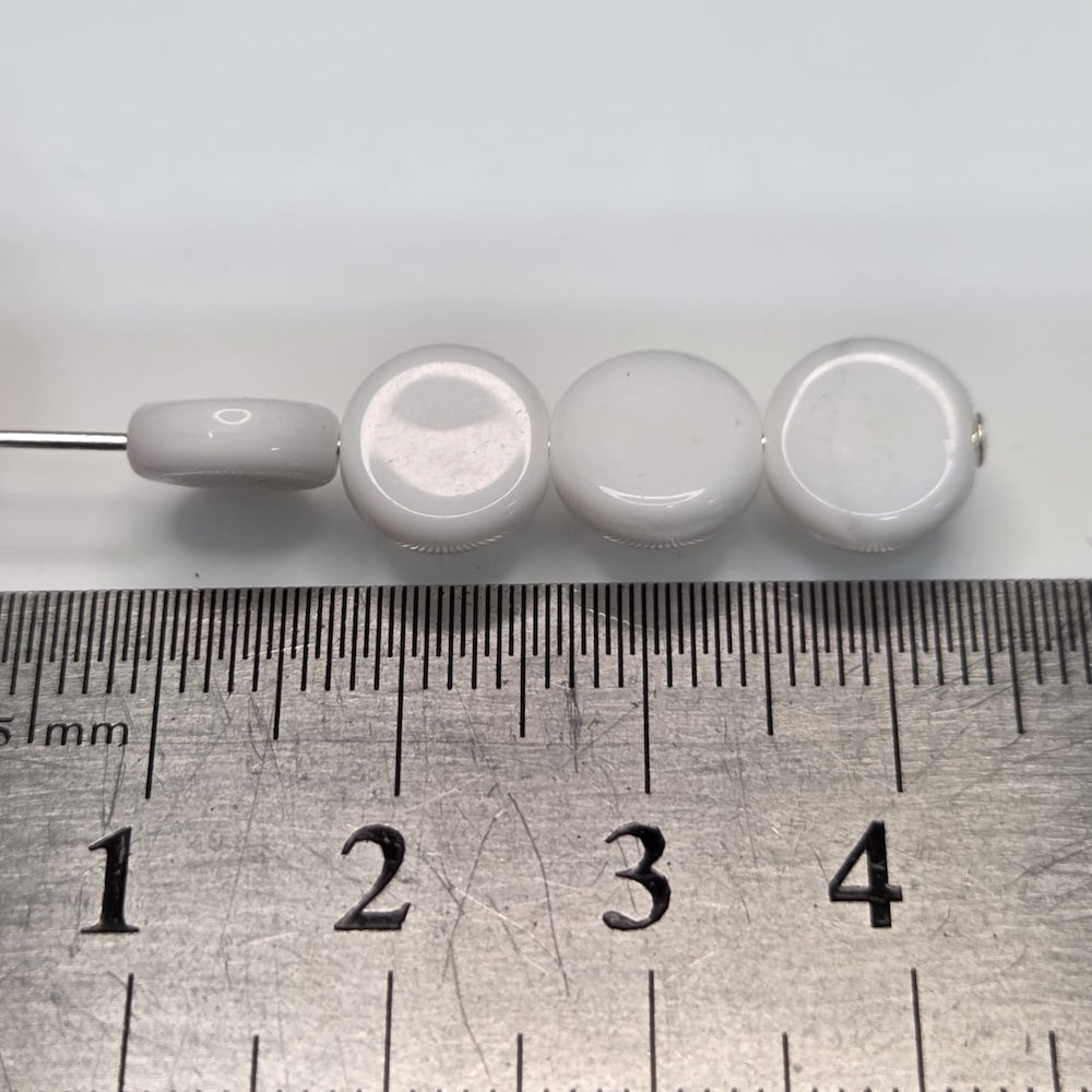 Close-up of white flat round beads with a glossy finish next to a ruler to show size
