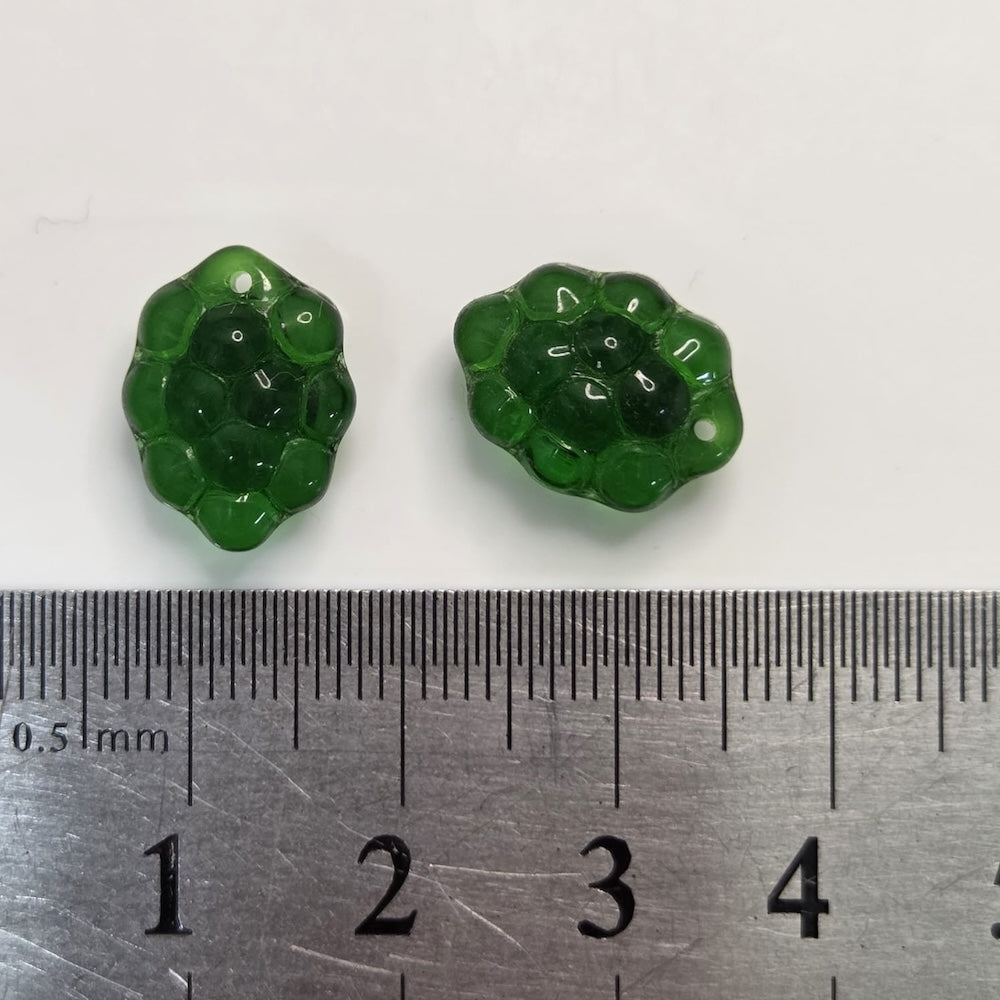 Two green floral beads next to a ruler for size reference on a white background