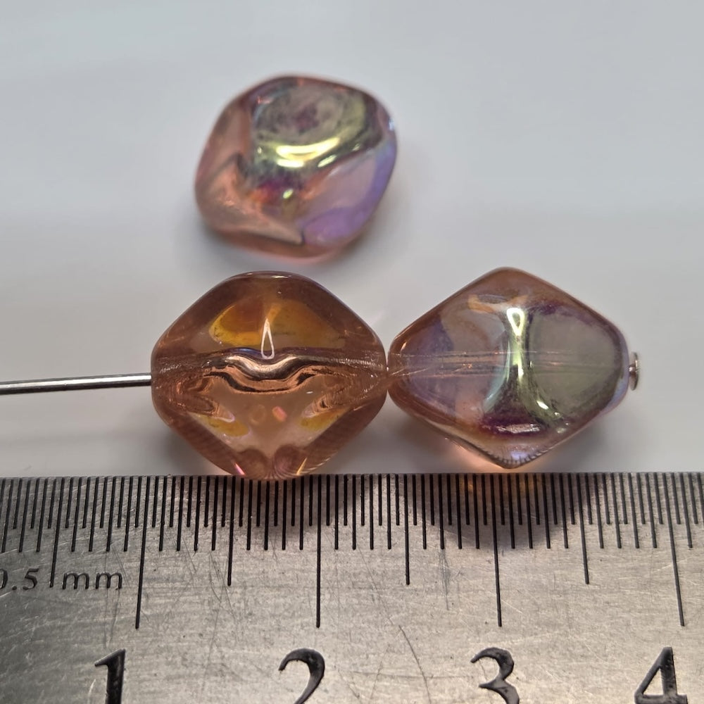 Close-up of transparent pink beads with shiny coating on parts of the surface with a ruler to show scale