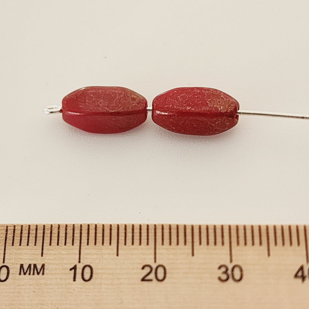 two red oval beads with a lustre surface threaded on a pin with a ruler to show sizing