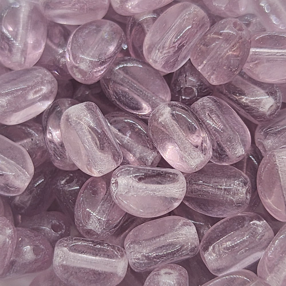 A close-up image of pinched rice-shaped Czech glass beads in a transparent light amethyst color.