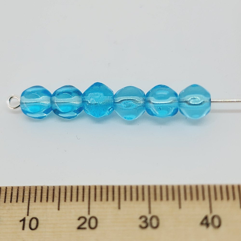 size blue glass beads threaded on a pin with a ruler to show scale