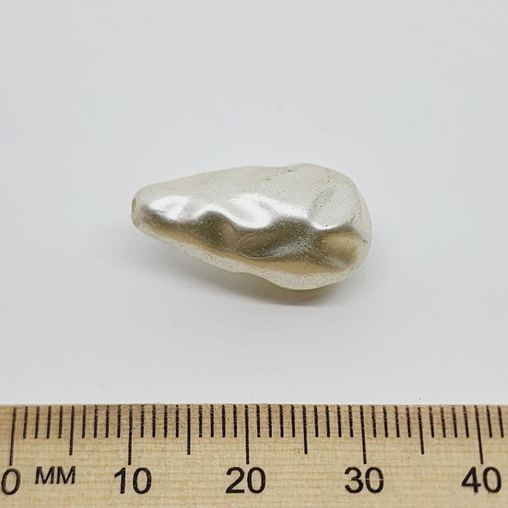 Pearl tear drop bead with a ruler for scale on a white background