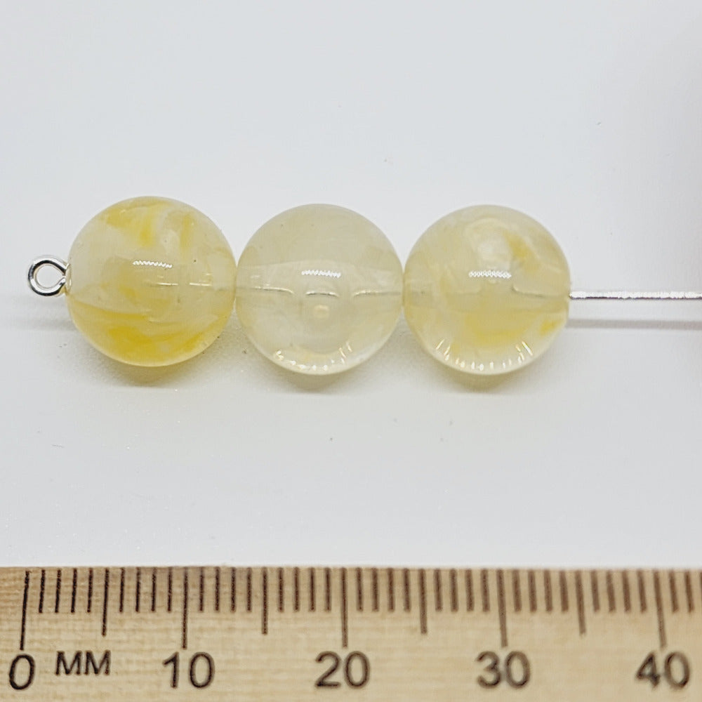 Citrine yellow gemstone look acrylic beads with visible threading holes for crafting jewelry on a white background against a ruler for scale