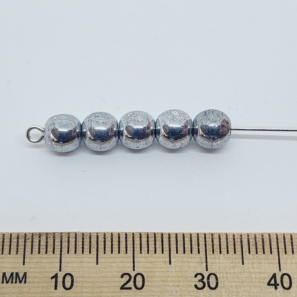 grey beads on a pin with a ruler to show scale