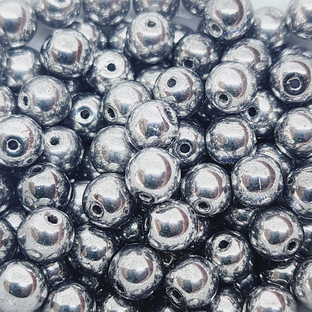A close-up image of small, round, grey transparent Czech glass beads with a silver lustre.