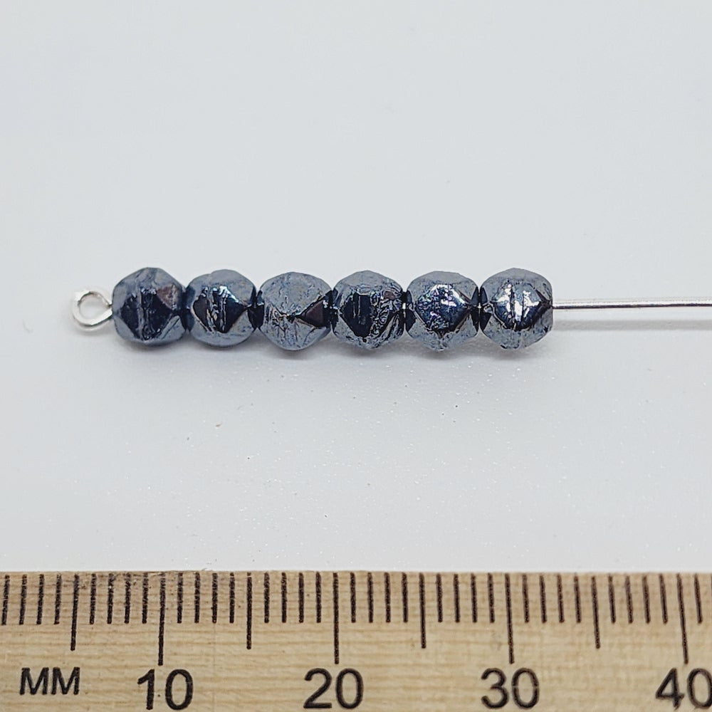 gunmetal grey facet beads on a pin with a ruler to show scale
