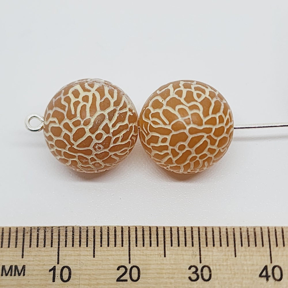 blue and white lucite round bead with a spider web type of patterning, showing visible holes for crafting jewelry next to a ruler to show scale