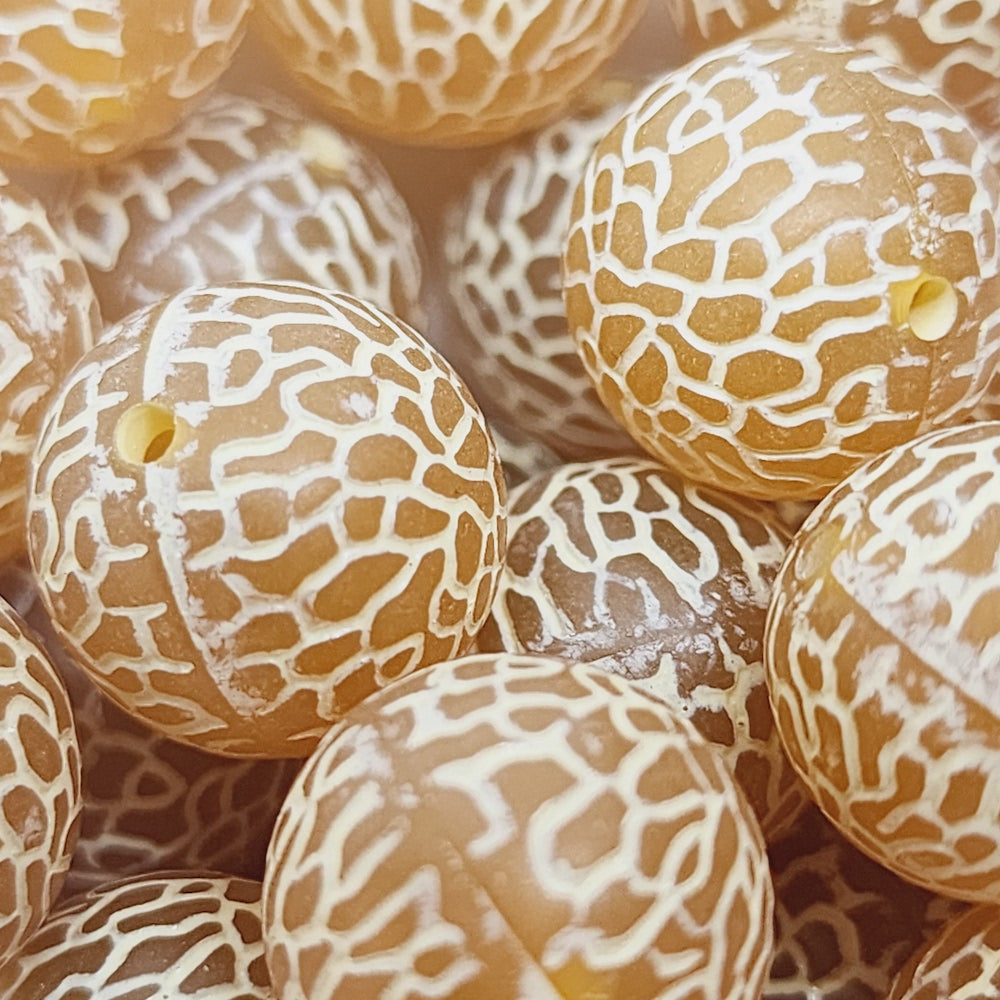 orange and white lucite round bead with a spider web type of patterning, showing visible holes for crafting jewelry