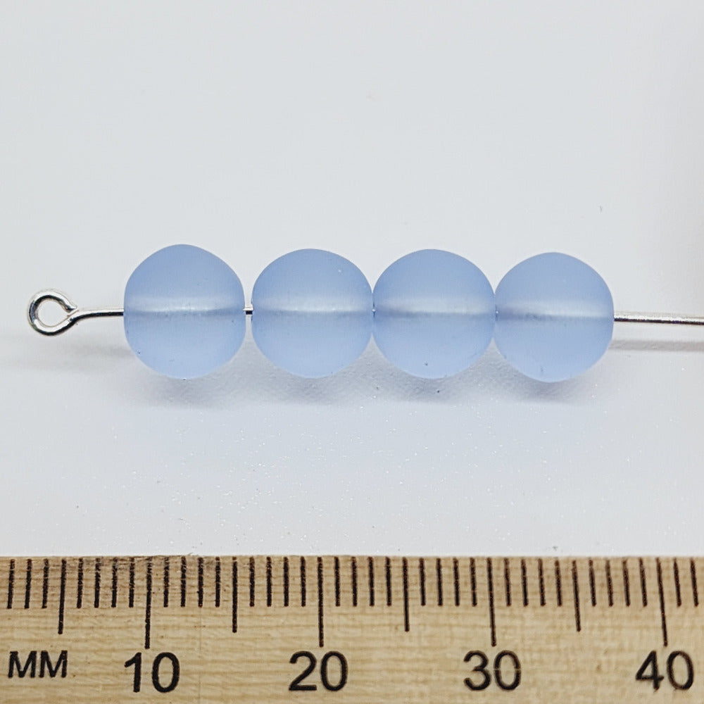 light blue frosted glass beads showing a threading hole for jewelery making threaded on a pin with a ruler to show scale