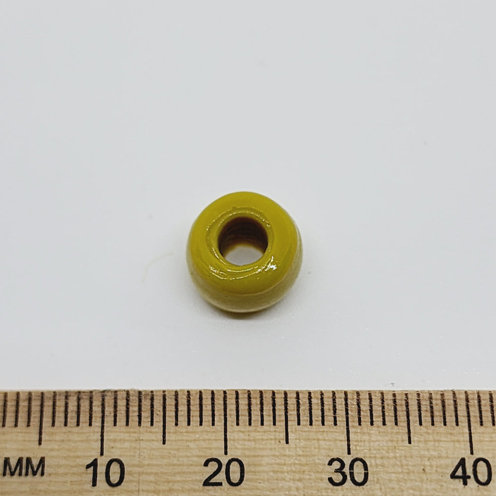 A large hole Indian glass bead on a white background using a wooden ruler for scale