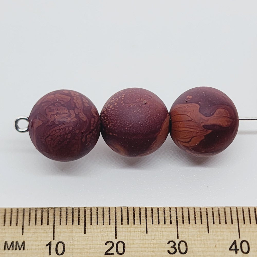 Three marbled brown beads with a ruler for scale on a white background