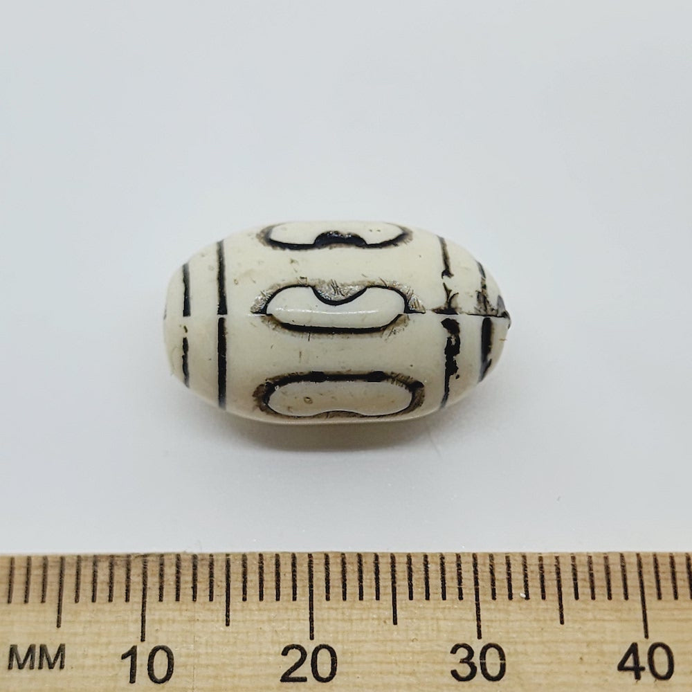 An oval-shaped vintage art deco style lucite bead with black etched designs and two lines of black around each end.