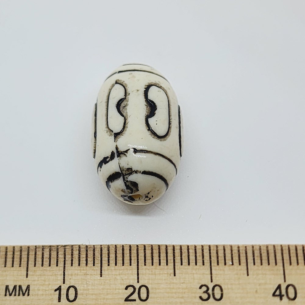 one vintage acrylic lucite beads with black etched designs, placed next to a ruler for scale.