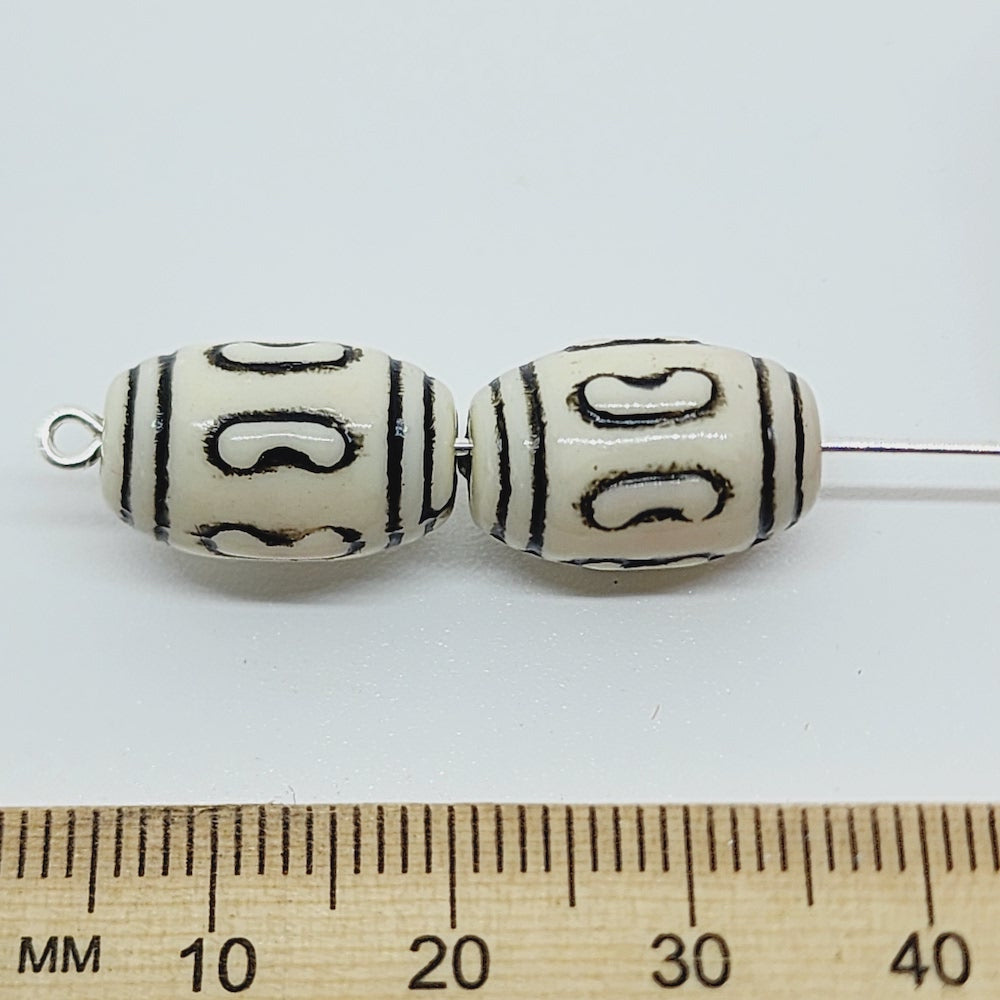 Two vintage acrylic lucite beads with black etched designs, placed next to a ruler for scale.