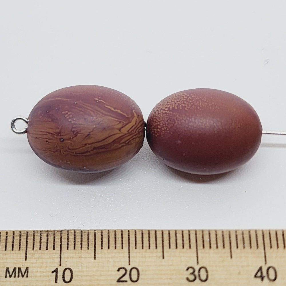 Two brown beads next to a ruler on a white background