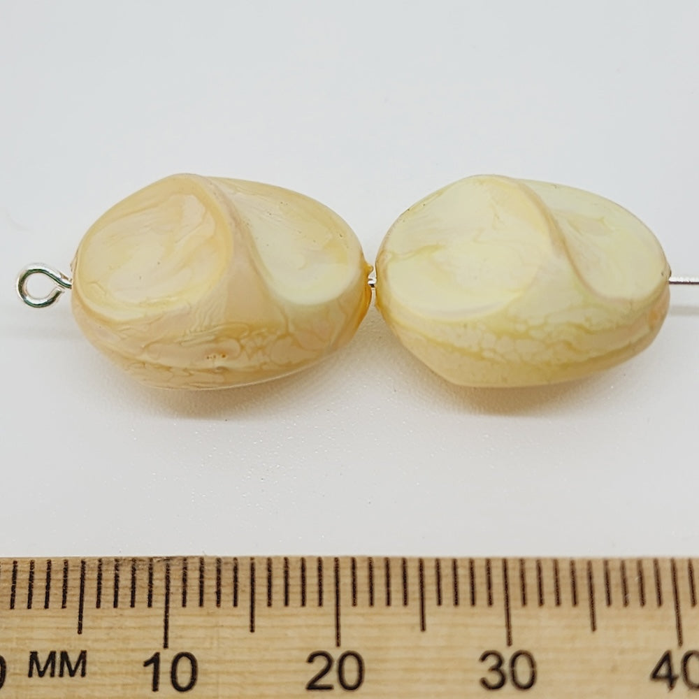 Two beige beads on a white background with a ruler for scale.