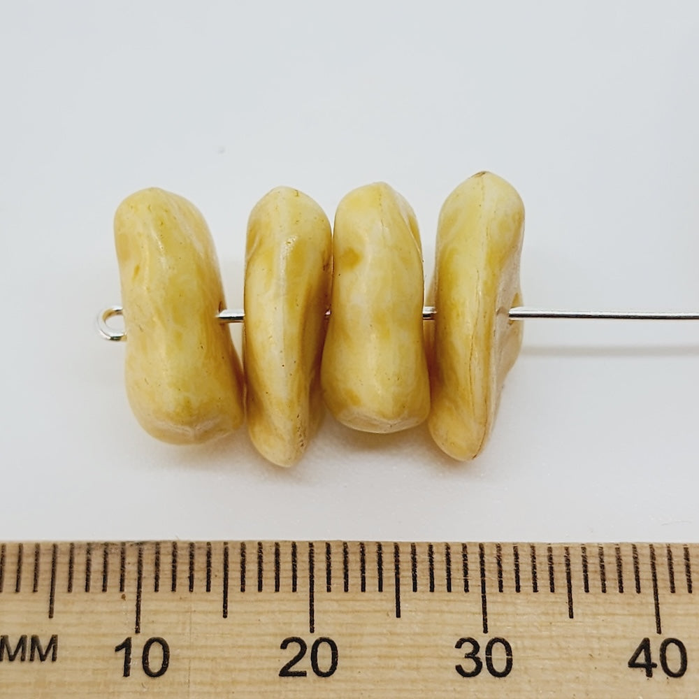 close up of foiur yellow stone look beads threaded on a pin to show direction of holes with a ruler to show scale