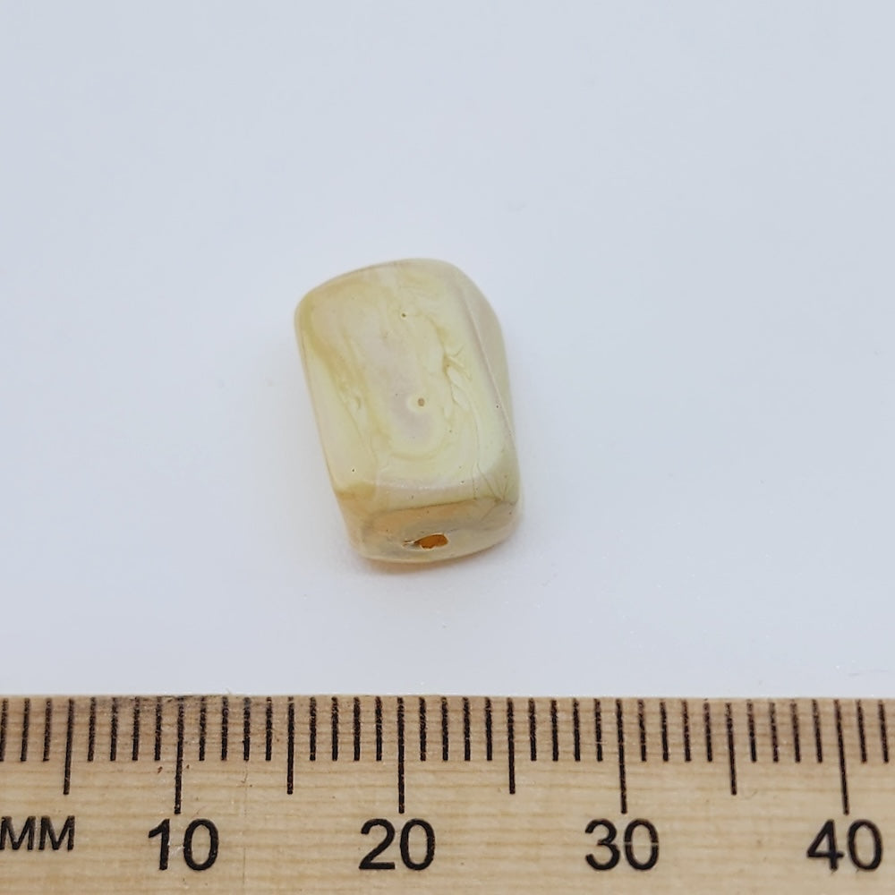 Beige cylindrical bead with a ruler for scale on a white background
