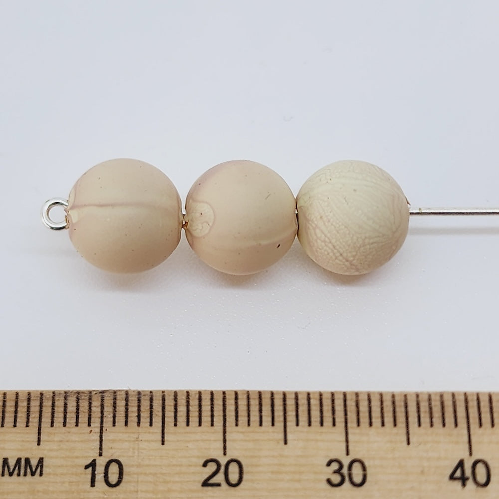Three beige beads on a white background with a wooden ruler for scale.