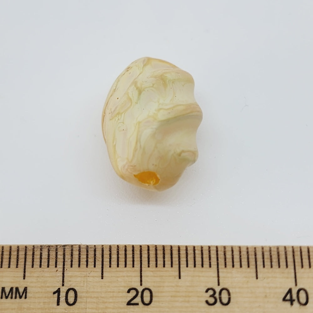 marbled surface beige bead with a ruler to show scale on a white background