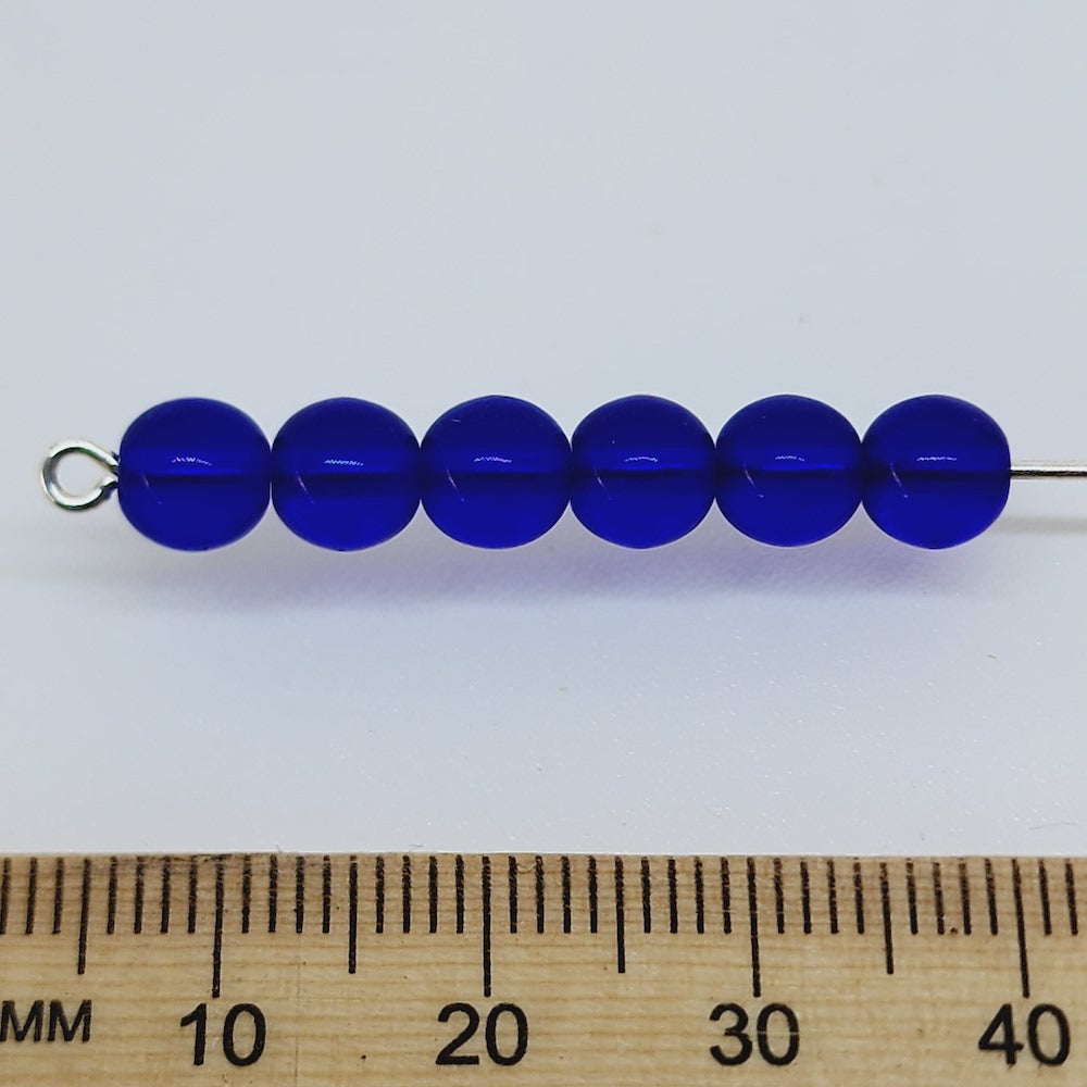 dark blue round glass beads on a pin with a ruler to show scale