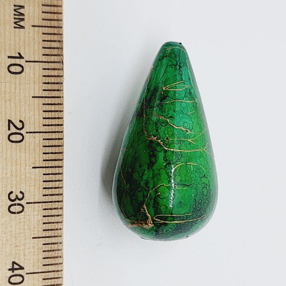 A teardrop-shaped vintage Lucite bead with a green bubble glaze look and gold drizzle patterns, next to a ruler for scale.