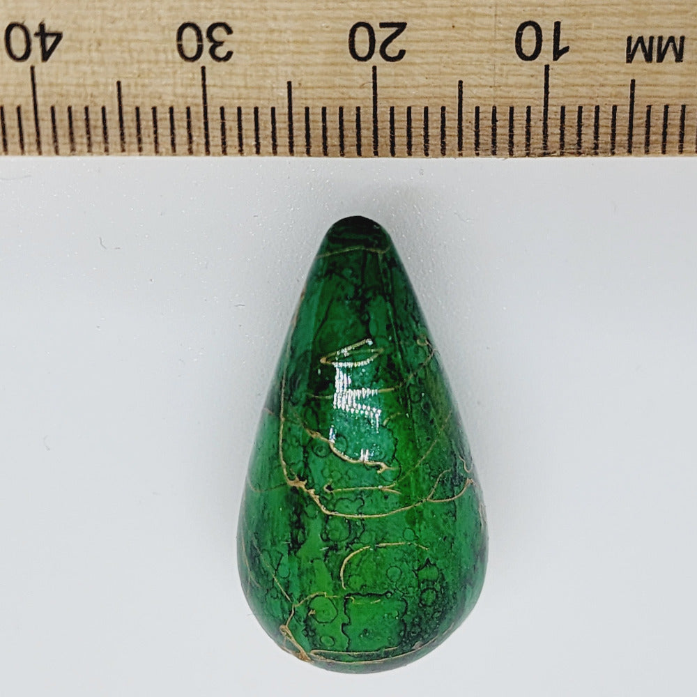 A teardrop-shaped vintage Lucite bead with a green bubble glaze look and gold drizzle patterns, next to a ruler for scale.