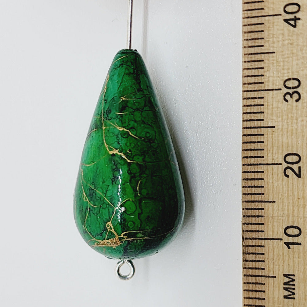 A teardrop-shaped vintage Lucite bead with a green bubble glaze look and gold drizzle patterns, next to a ruler for scale.