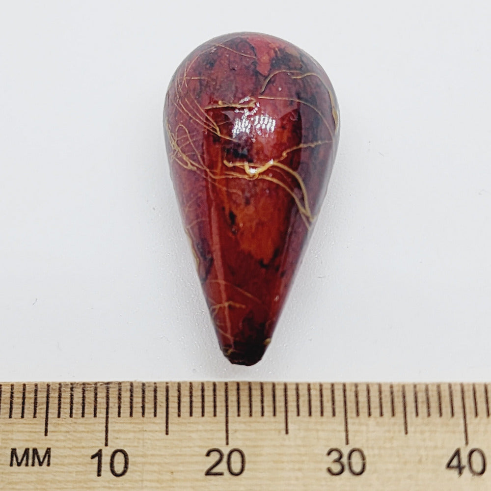 A teardrop-shaped vintage Lucite bead with a rust bubble glaze look and gold drizzle patterns, next to a ruler for scale.