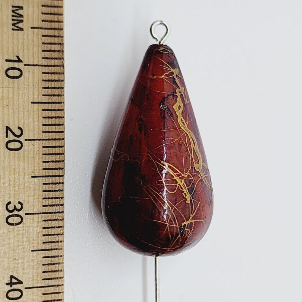 A teardrop-shaped vintage Lucite bead with a rust bubble glaze look and gold drizzle patterns, next to a ruler for scale.