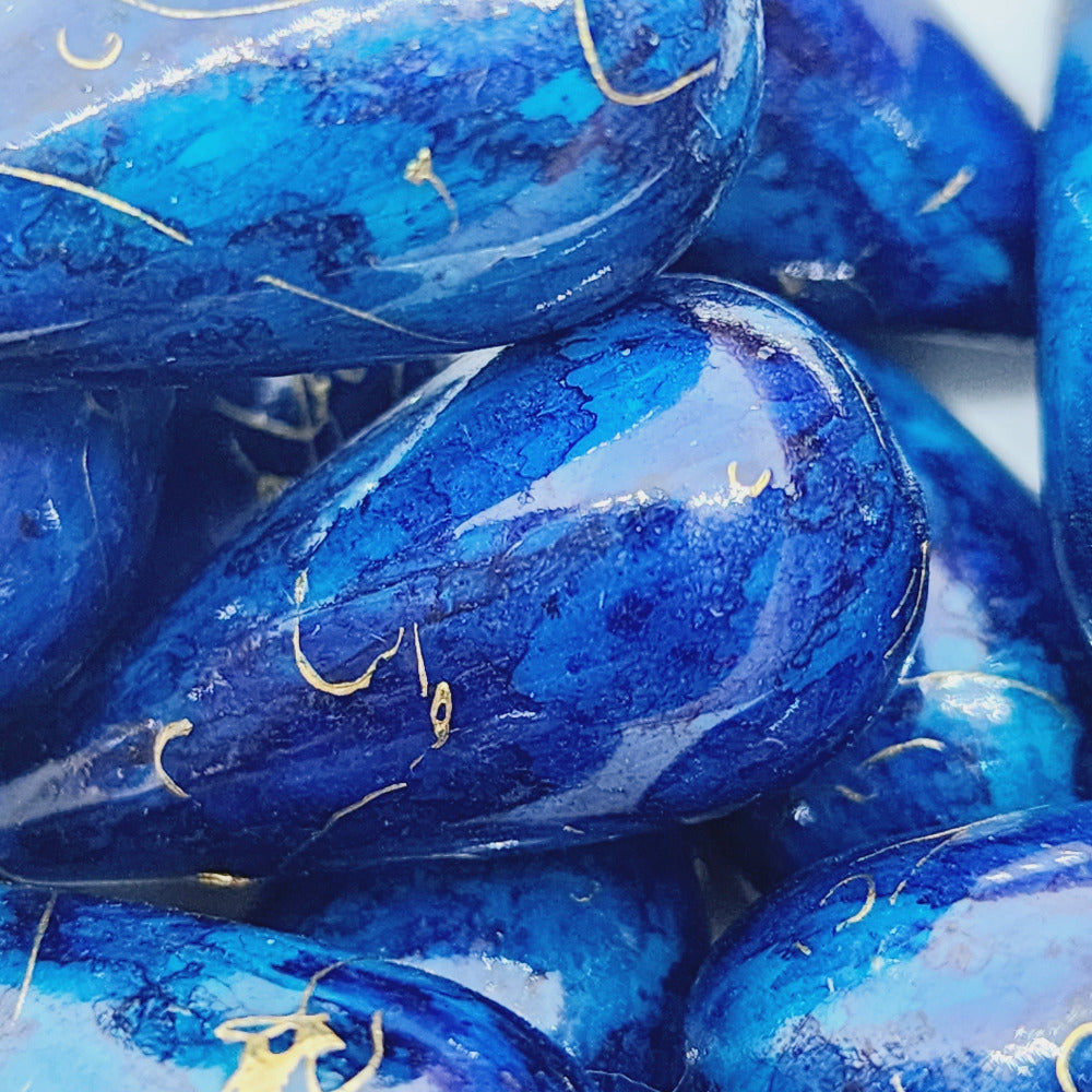 A group of teardrop-shaped vintage Lucite bead in blue with a gold drizzle pattern,