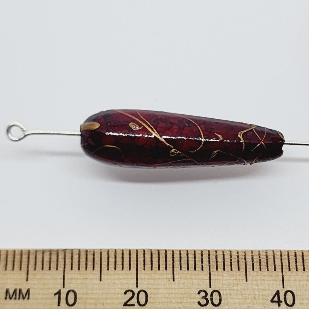 A teardrop-shaped vintage Lucite bead with a brown bubble glaze look and gold drizzle patterns, next to a ruler for scale.