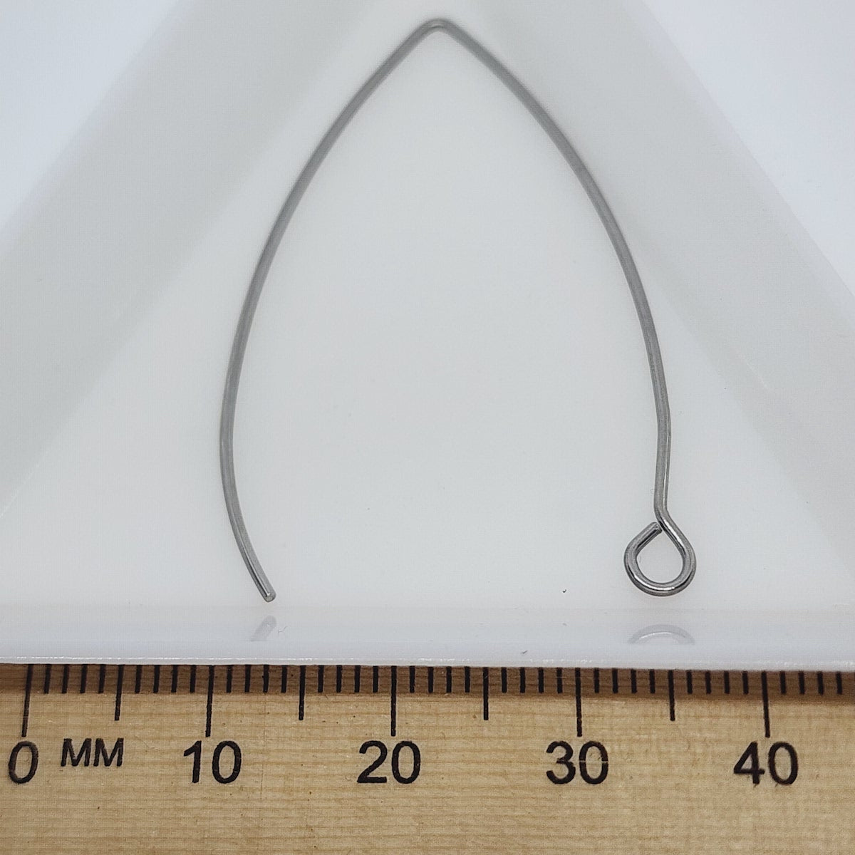 close up of one large silver anti tarnish ear wire with a white background with a wood ruler for scale