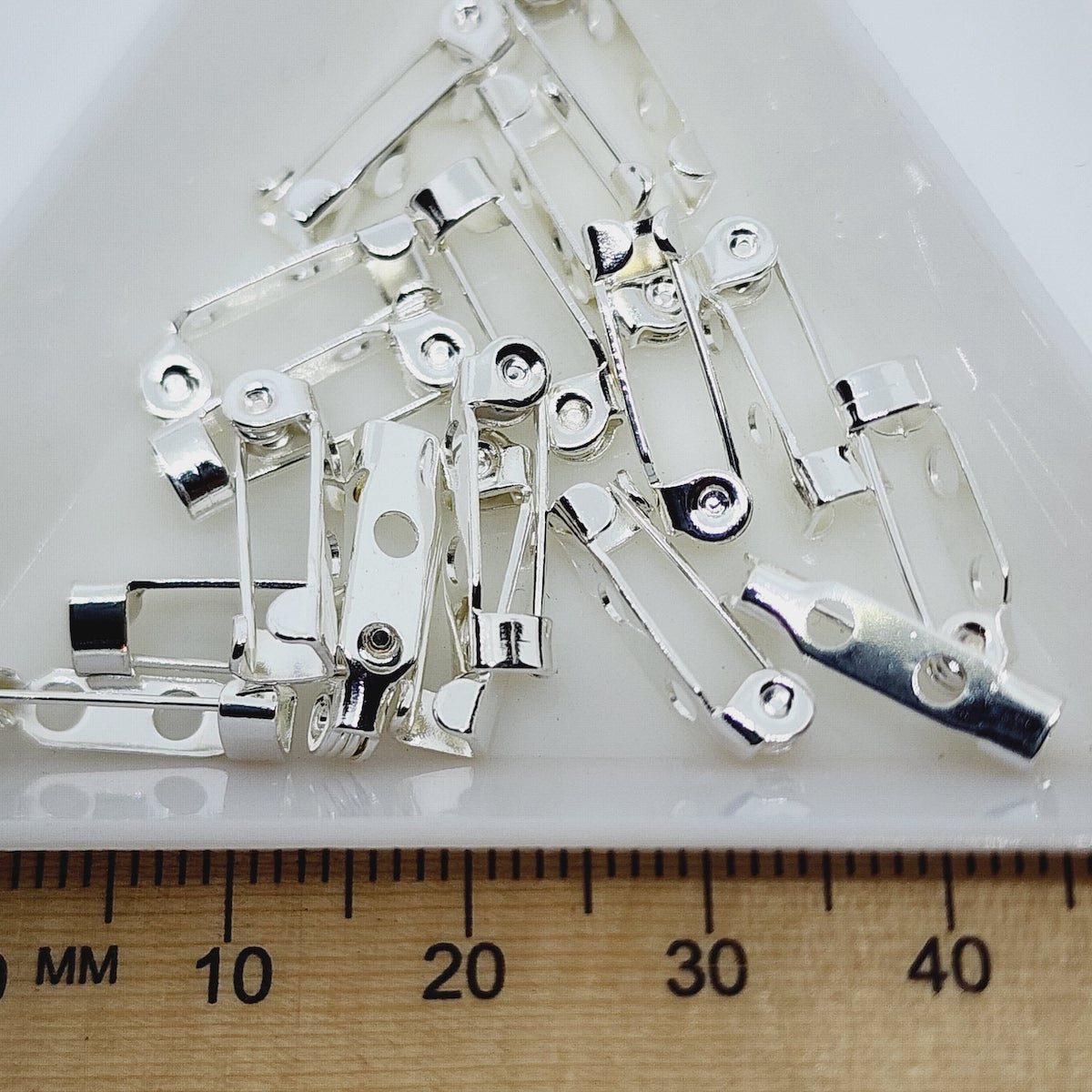 silver brooch backs displayed in a white dish with a wooden ruler for scale