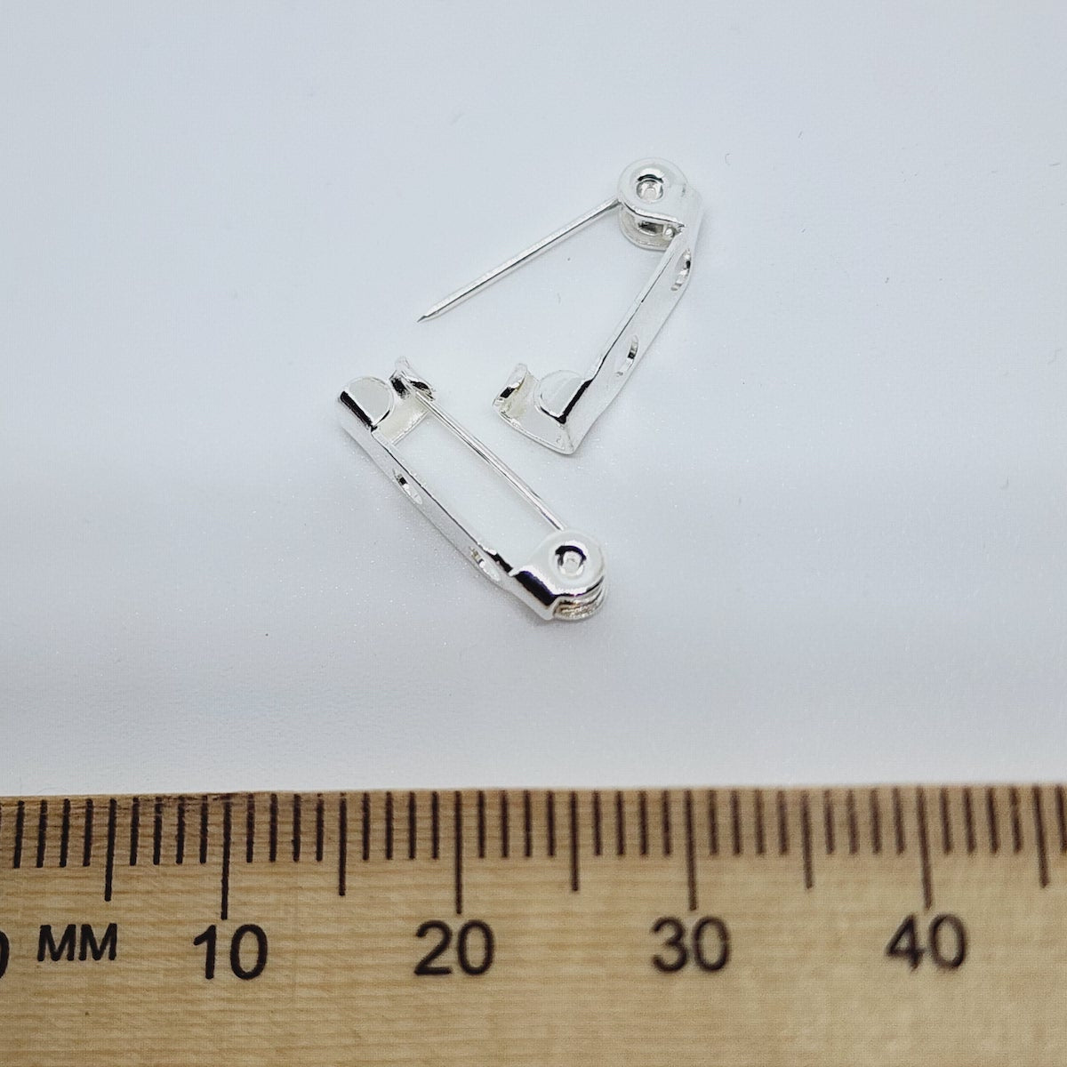 Silver brooch pin on a white background with a wooden ruler for scale.