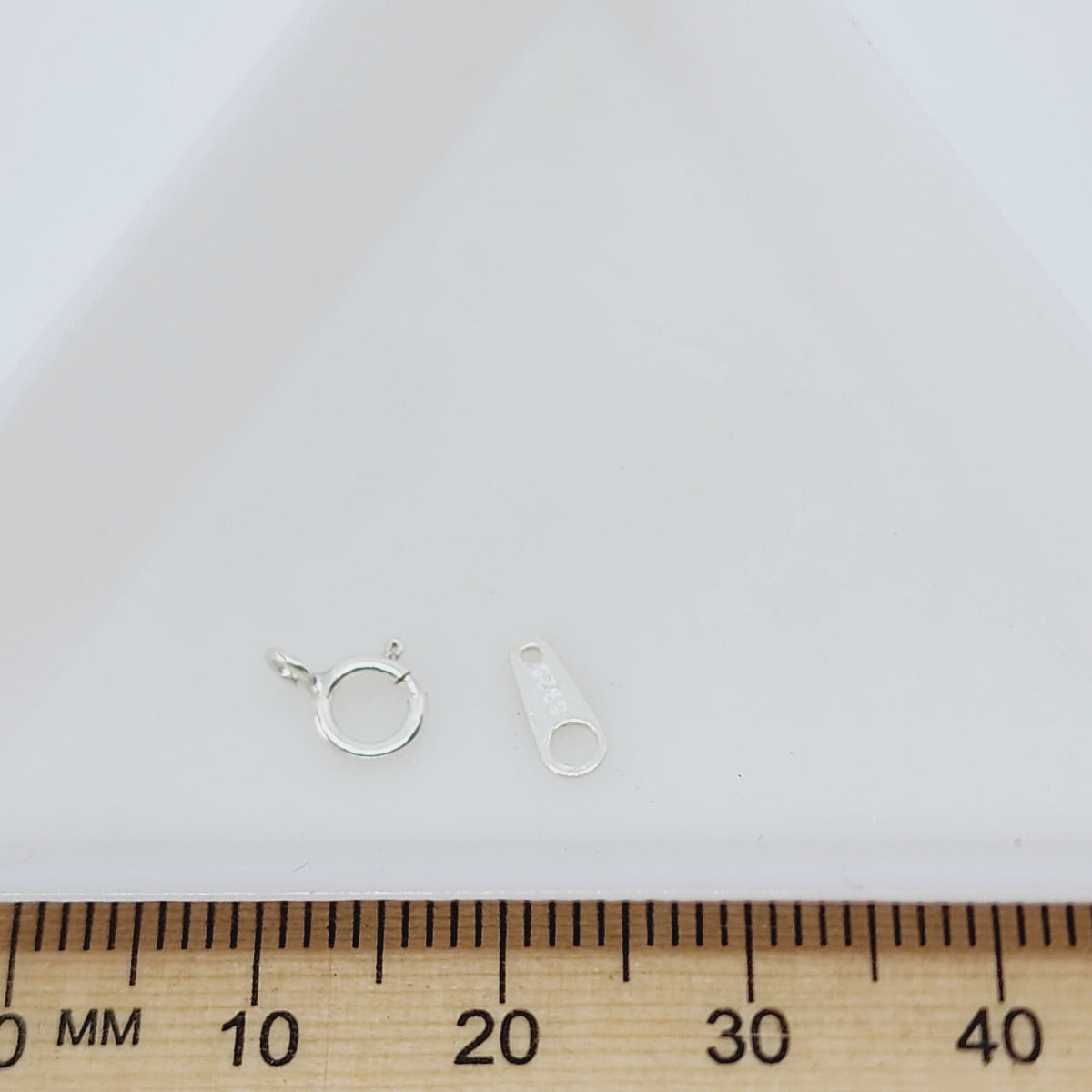 a small round bolt style clasp with an end tag for attaching to hand made jewelry pieces plated in 925 sterling silver with a wood ruler to show scale