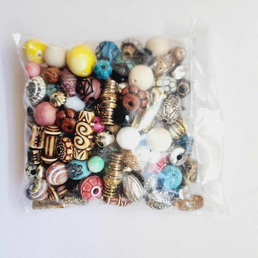 A clear plastic bag filled with assorted decorative beads and charms in many colors and patterns, photographed on a plain white background.