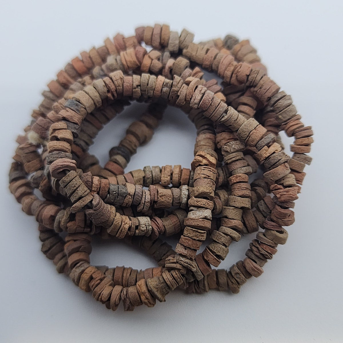 A collection of brown terracotta-colored faience beads arranged in a loop, with varying shapes and textures.