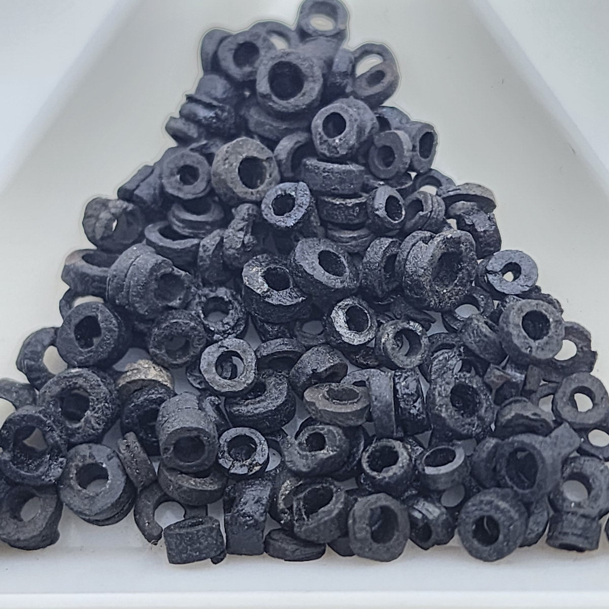A close up photo of a collection of black vintage faience clay beads on a white background showing different shapes and sizes with a clear look at the threading holes and quality