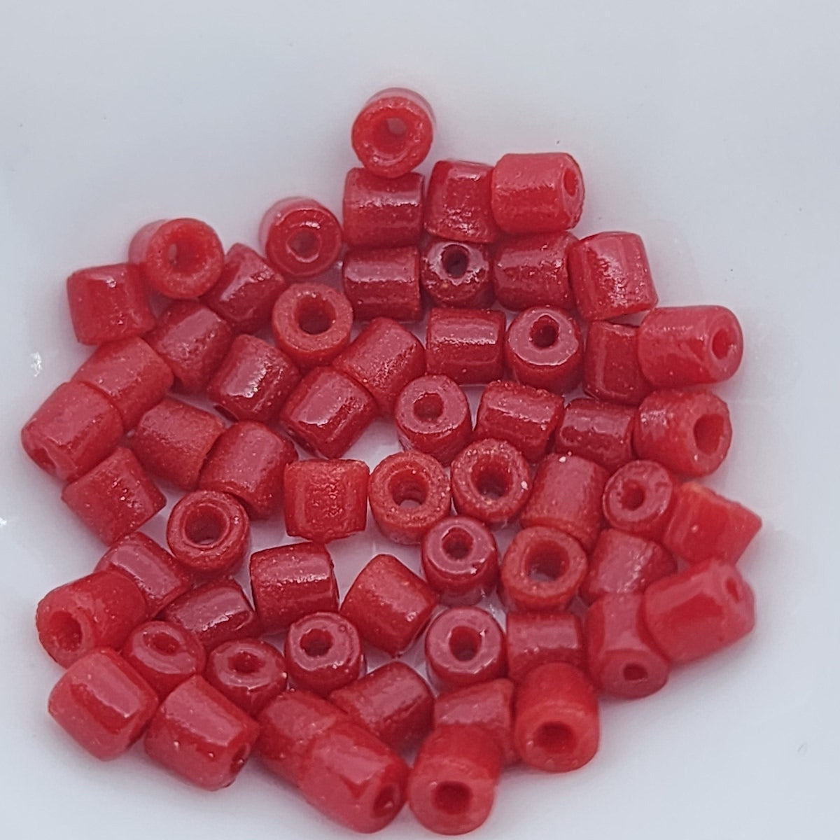 A collection of vintage Egyptian red cylindrical glass beads made from powdered glass with visible holes for stringing, on a light background showing visible holes for stringing