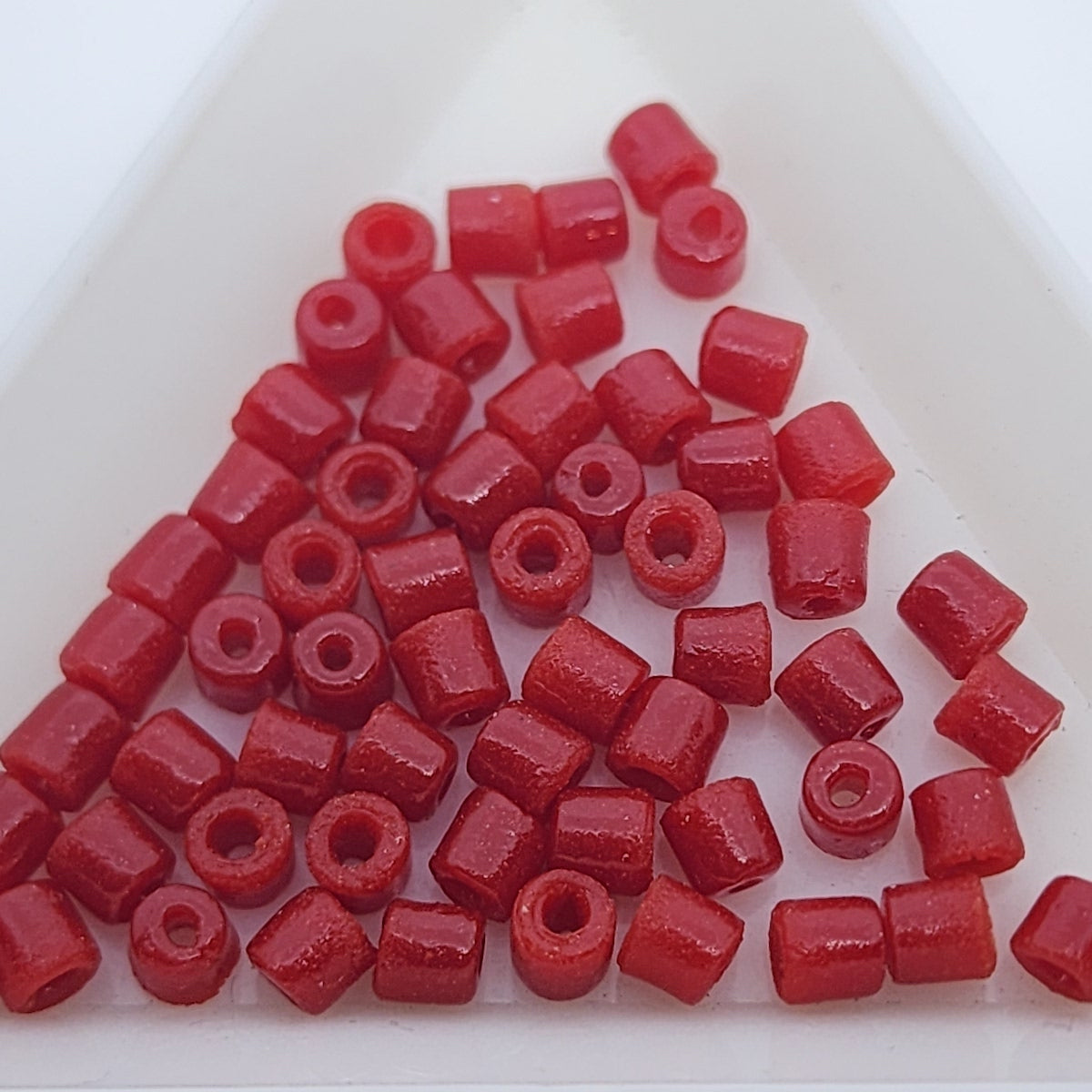 A collection of vintage Egyptian red cylindrical glass beads made from powdered glass with visible holes for stringing, on a light background showing visible holes for stringing