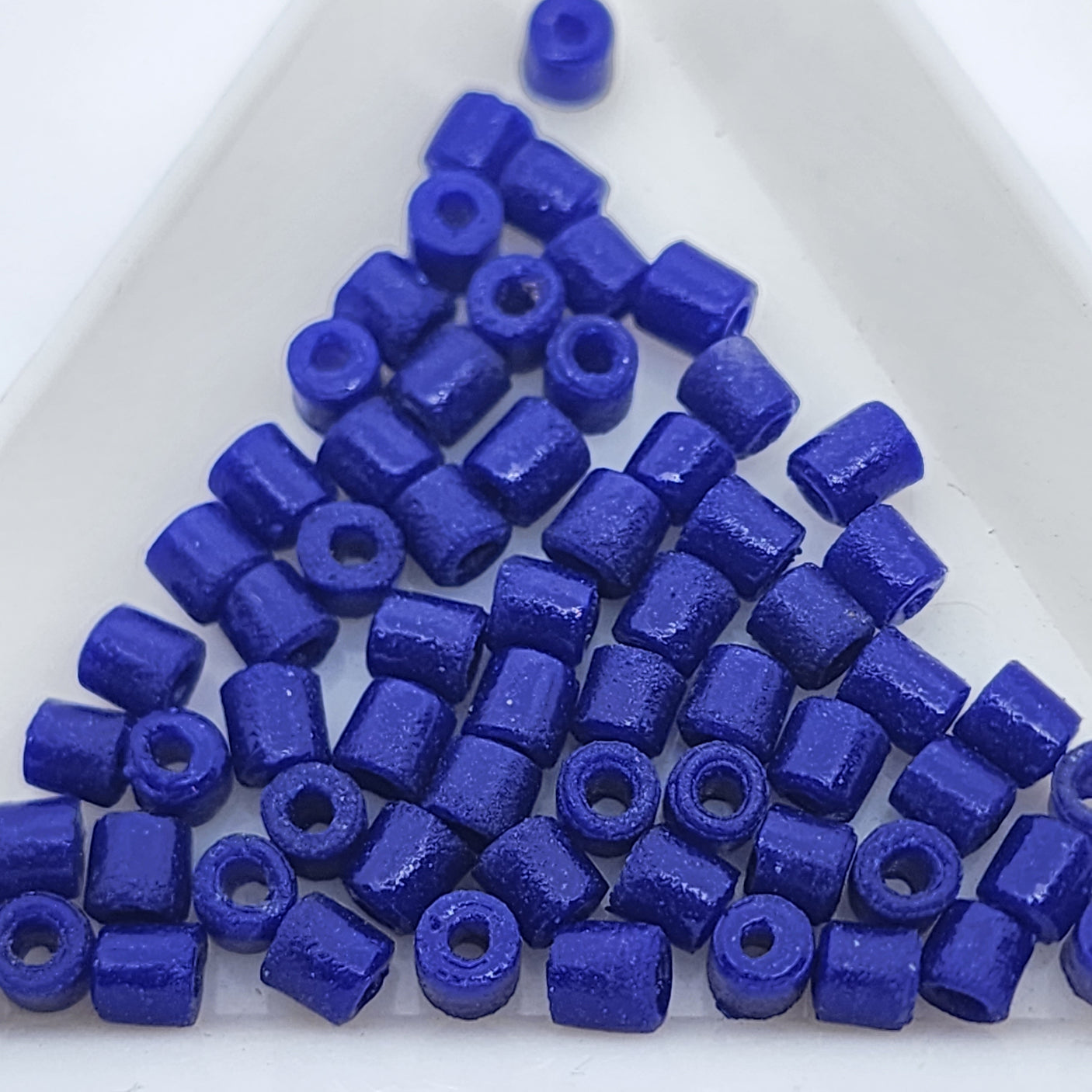 A collection of vintage Egyptian lapis lazuli blue cylindrical glass beads made from powdered glass with visible holes for stringing, on a light background.