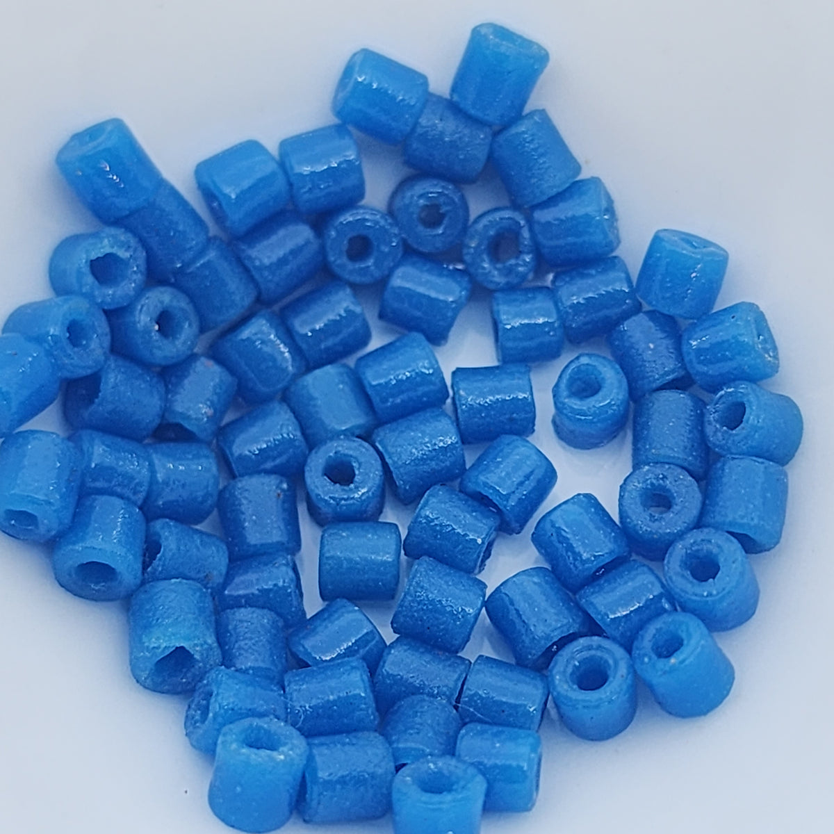 A collection of vintage Egyptian dark blue cylindrical glass beads made from powdered glass with visible holes for stringing, on a light background.