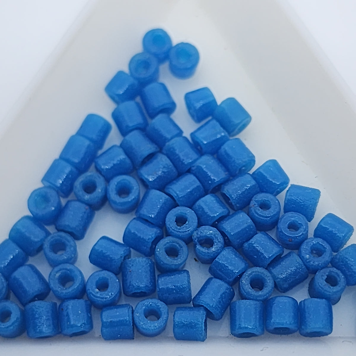 A collection of vintage Egyptian dark blue cylindrical glass beads made from powdered glass with visible holes for stringing, on a light background.