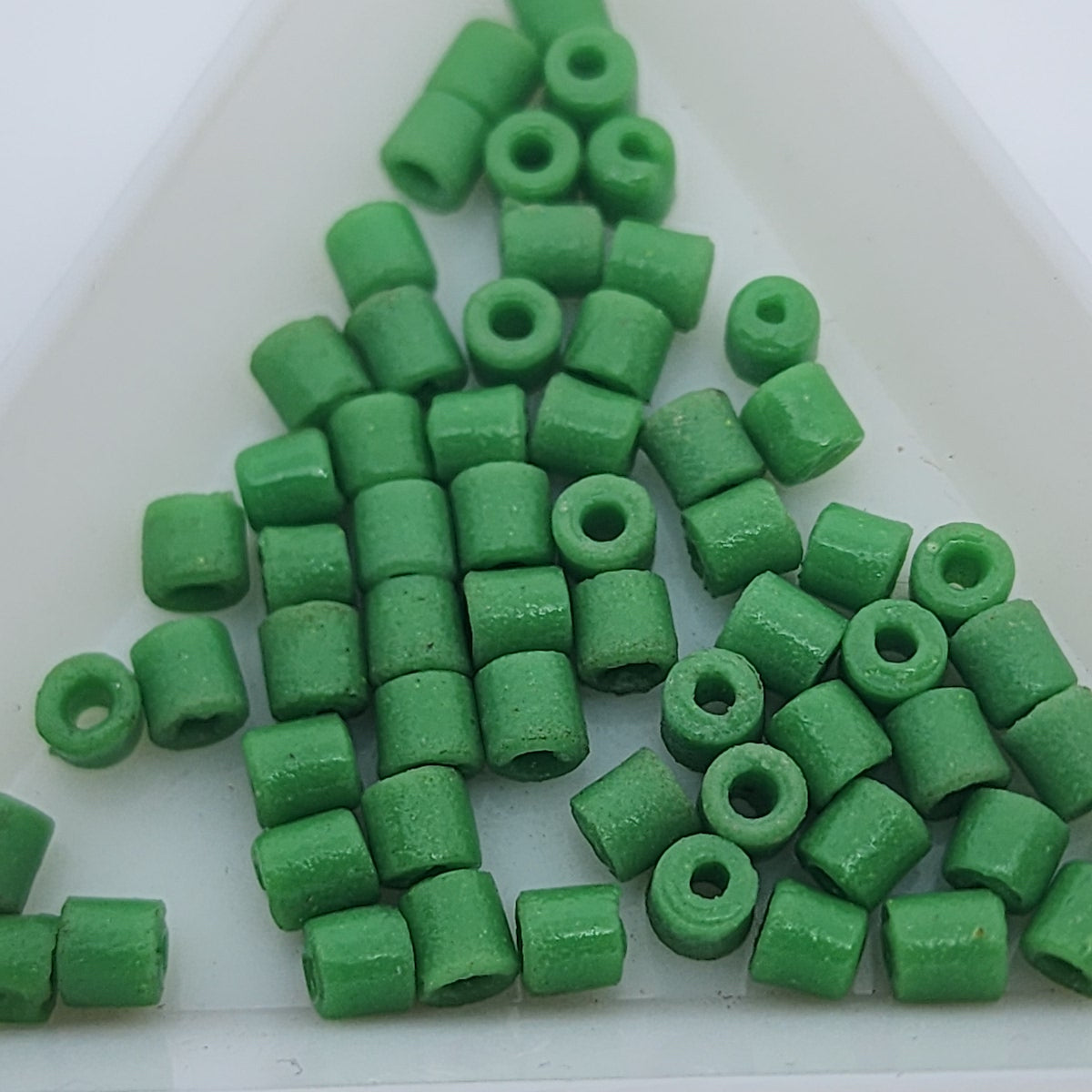A collection of vintage Egyptian green cylindrical glass beads made from powdered glass with visible holes for stringing, on a light background.