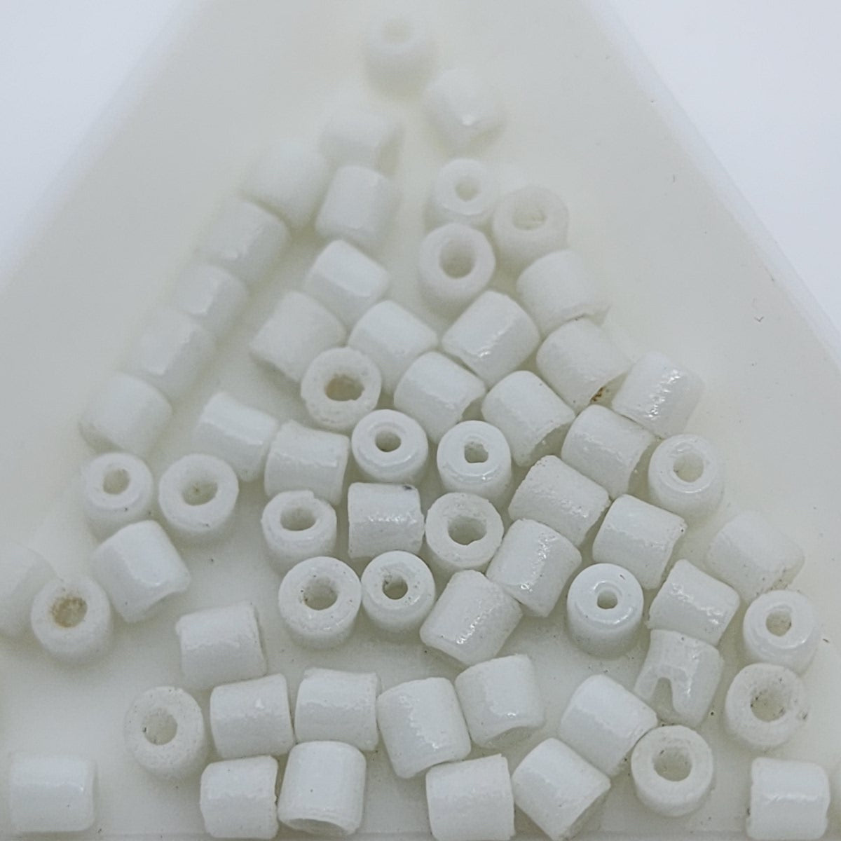 A collection of vintage Egyptian white cylindrical glass beads made from powdered glass with visible holes for stringing, on a light background.