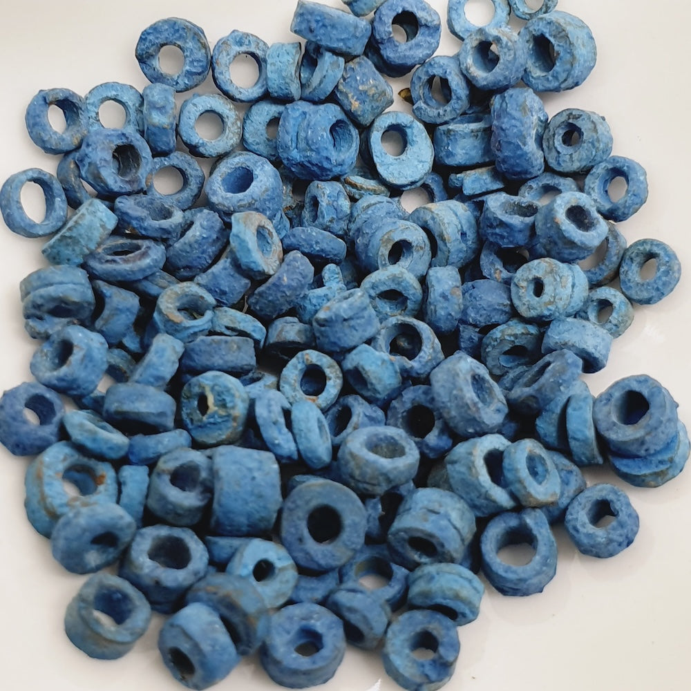 A close up photo of a collection of turquoise blue vintage faience clay beads on a white background showing different shapes and sizes with a clear look at the threading holes and quality