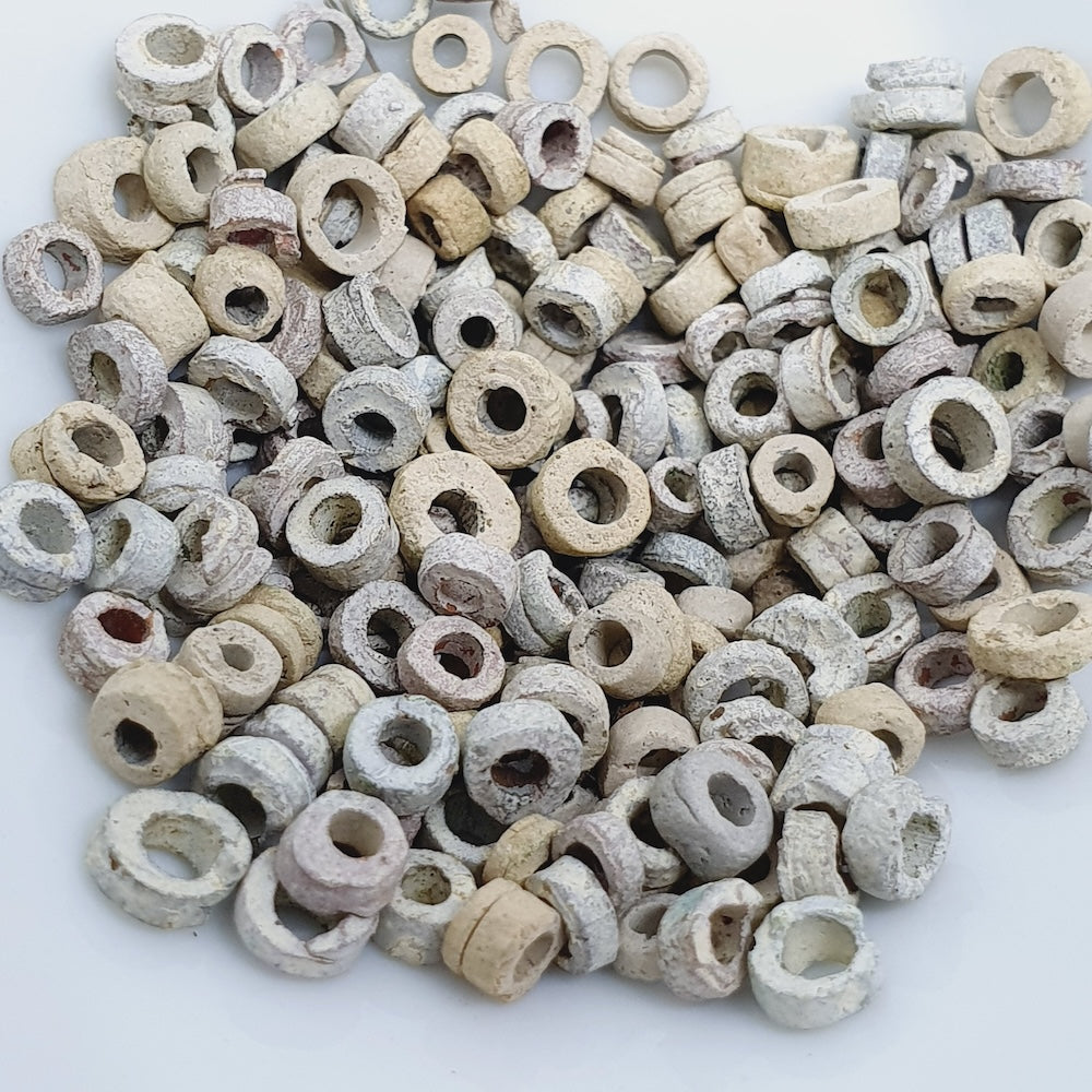 A close up photo of a collection of cream off white vintage faience clay beads on a white background showing different shapes and sizes with a clear look at the threading holes and quality